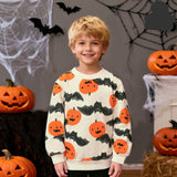 A young boy smiling and wearing a long-sleeve crewneck sweatshirt with an orange pumpkin and black bat pattern, posed in a Halloween-themed setting with jack-o'-lanterns, cobwebs, and black bat decorations.